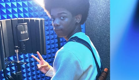 Boy in soundbooth with blue light and recording equipment.